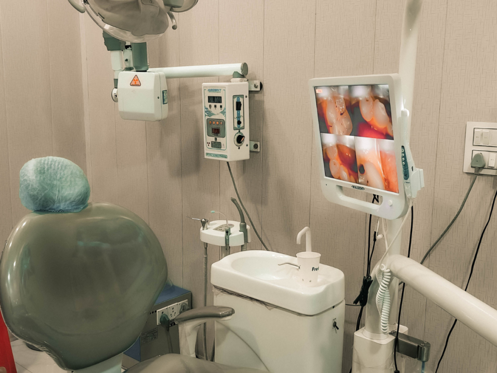 Dental examination room with a chair, monitor showing intraoral images, and X-ray equipment.