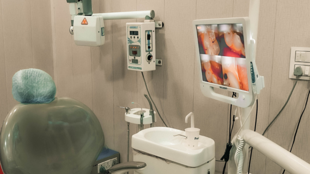 Dental examination room with a chair, monitor showing intraoral images, and X-ray equipment.